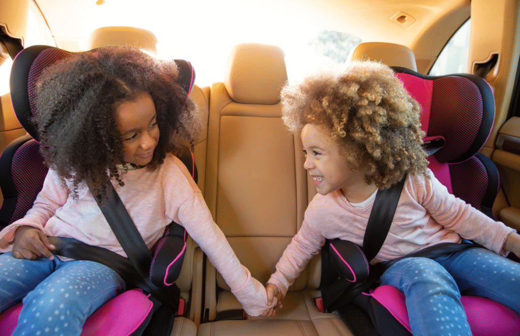 Two kids girls holding hands sitting safely on a car seat wearing seatbelts