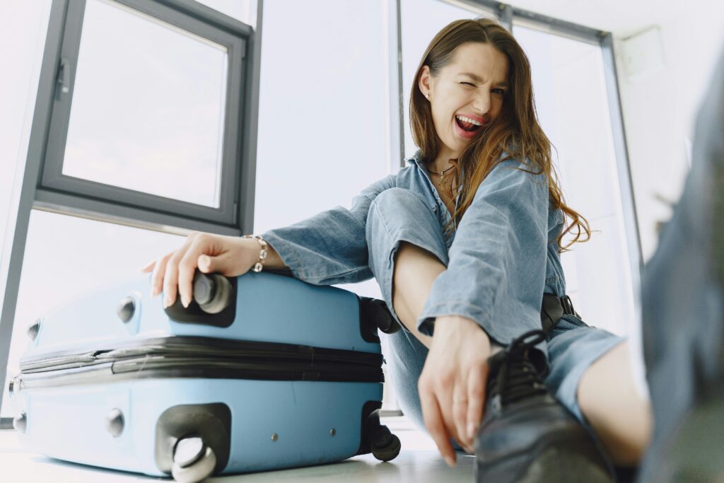 Cheerful trendy young woman sitting on floor with luggage - Budget Travel Tips
