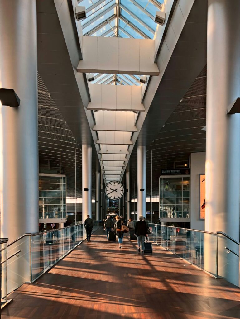 People walking in an airport aisle with a big clock - Budget Travel Tips