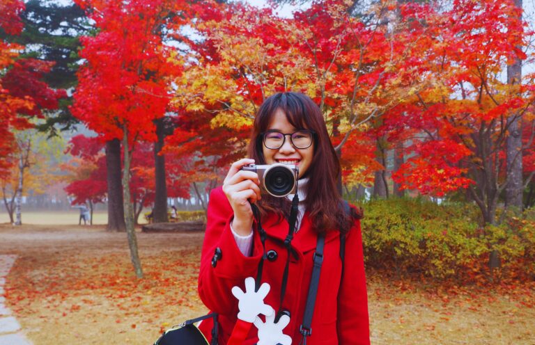 Free Attractions and Activities - Featured Image - tourist holding a camera in a city park with many trees in red autumn leaves