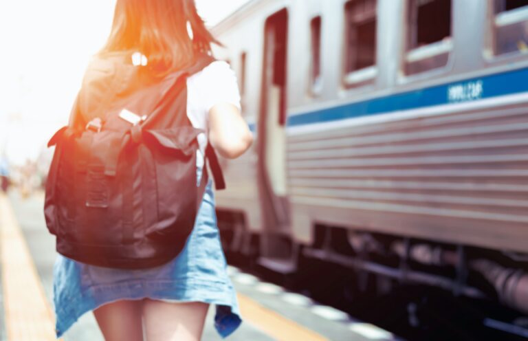 Public Transport for Travelers - a young woman carrying a black backpack. She is walking towards a train and about to get on baord.