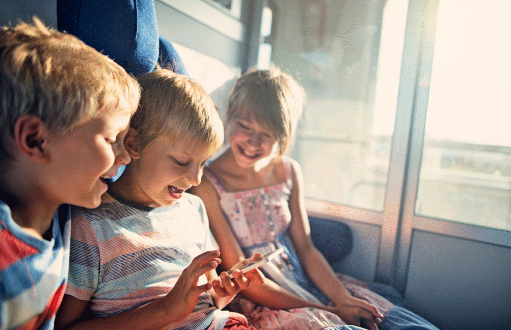Kids traveling by train. Little girl and two boys are smiling and playing with smartphone. The smartphone is turning a boring trip into fun.