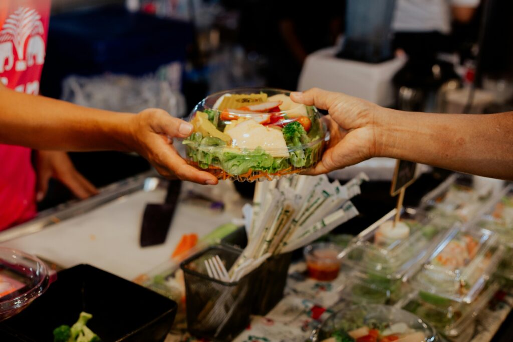 Cheap Travel Food Tips - Healthy Food - Person Handing Over A Packed Vegetable Salad in Plastic Container