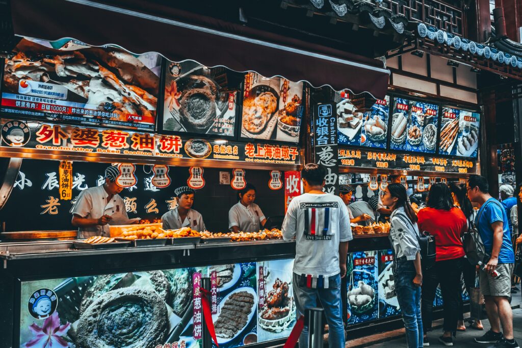 Cheap Travel Food Tips - Street Food - Street food stalls in Shanghai, China. Tourists are busy choosing from the food menus.