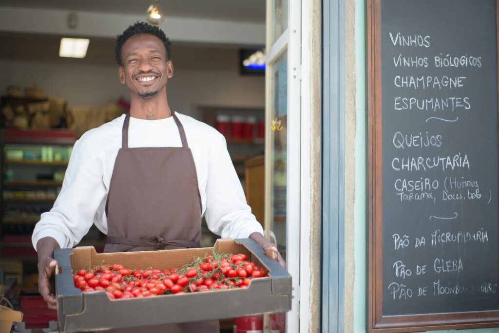 ood Travel Hacks - Ask the Locals - A vendor smiling while holding a box of fruits that he sells in their local supermarket