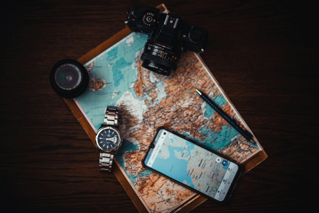 Traveletty - Best Free Travel Apps - Google Maps app opened in a phone on top of a traditional map with other travel essentials