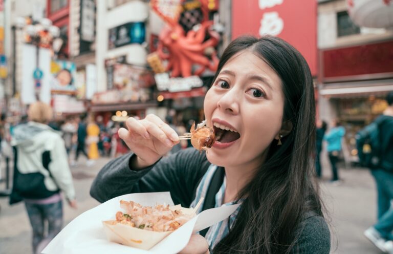 Traveletty - Budget Travel Food Tips - Featured Image - A young female traveler eating street food
