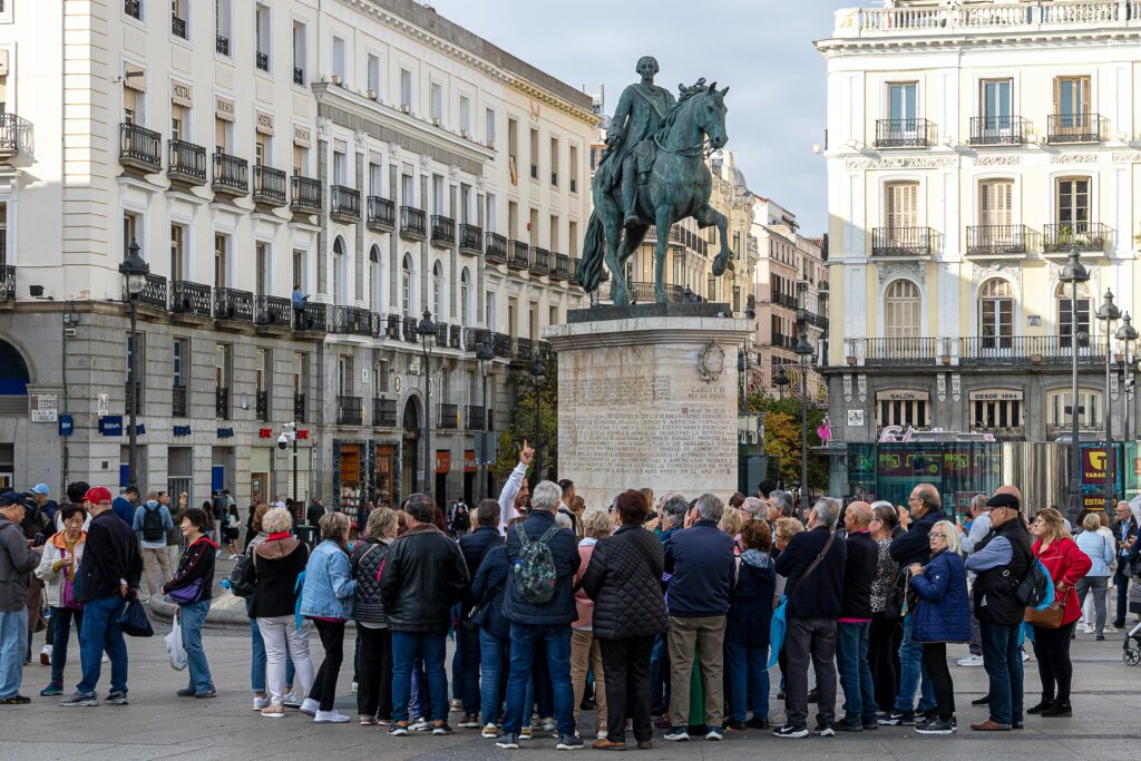 Traveletty - Free Walking Tours - A group of tourists gather at the iconic Puerta del Sol in Madrid while listening to a free walking tour guide