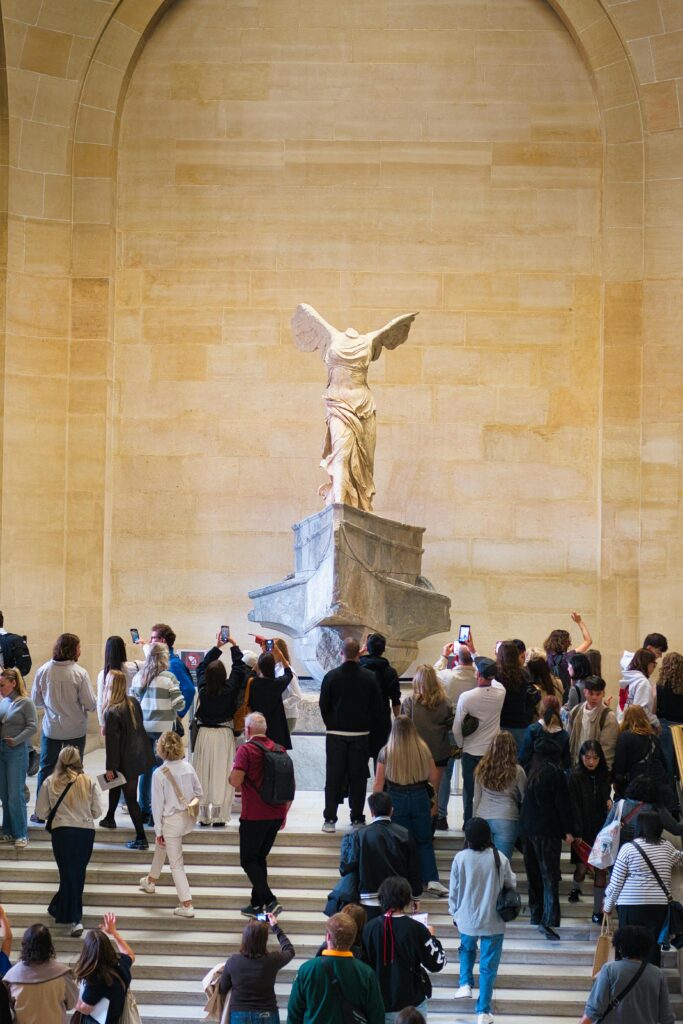 Traveletty - Museums and Art Galleries - Crowd admiring the winged victory of Samothrace inside a museum