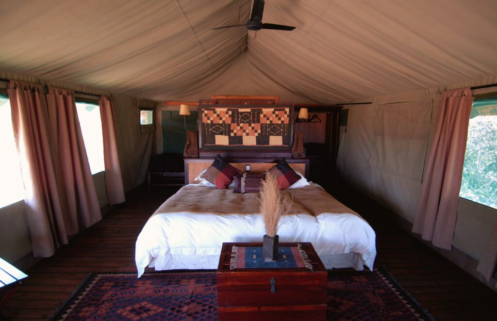 Traveletty - Safari Tents Interior - A luxurious safari Tent in Botswana, Africa is complete with a bed, a chest, lamps and other furniture.