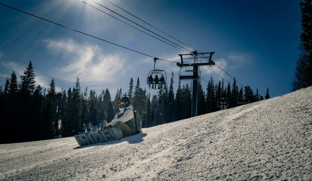 Traveletty - Ski Resorts - a person with a snowboard sitting on the snow covered slope under a ski lift
