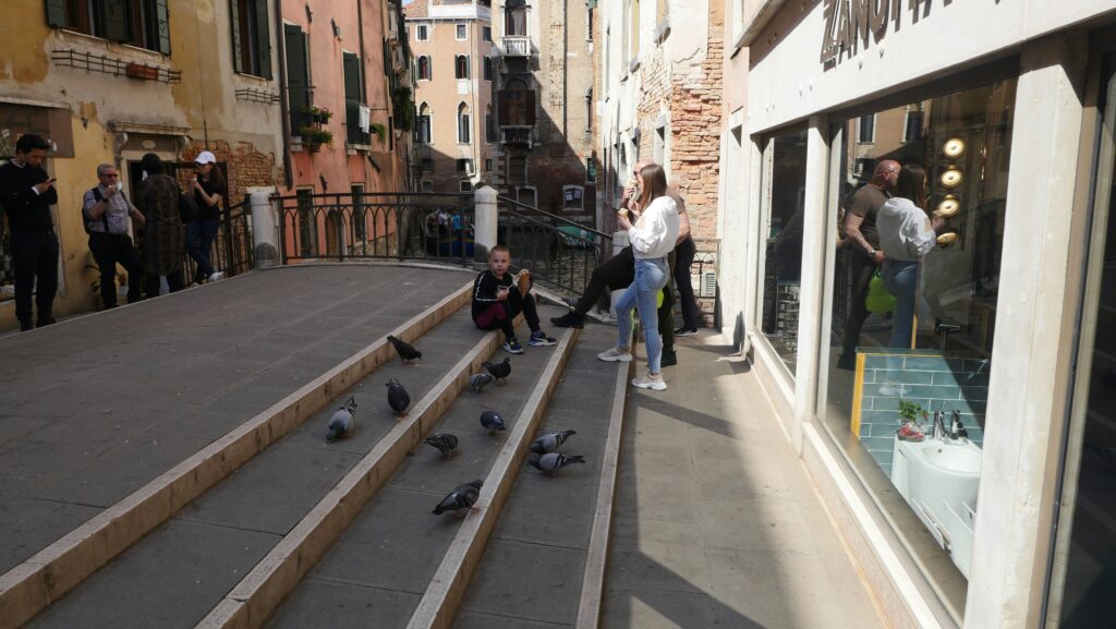 Traveletty - Travel Etiquette and Safety - a group of tourists standing by the steps outside a local store that has many pigeons in Venice Italy