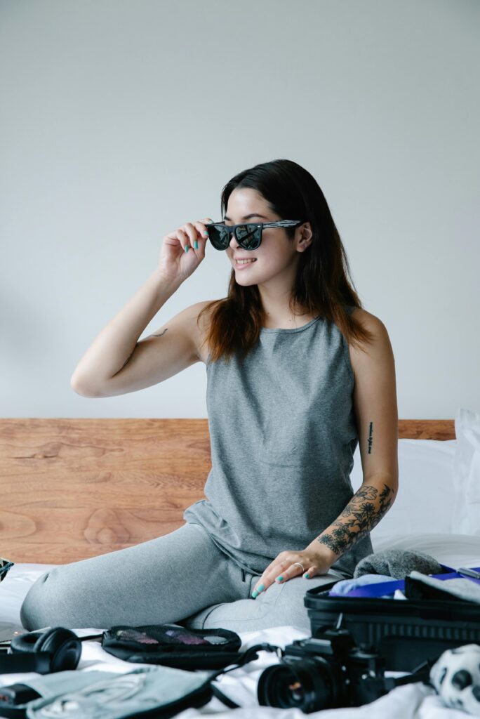 Traveletty - Travel Health and Safety - a woman in gray tank top wearing black sunglasses while getting ready of her things to travel