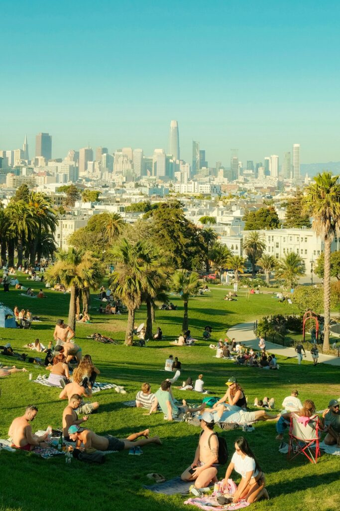 Traveletty - Urban Parks for Picnicking - People relaxing and having picnic on a grassy hill overlooking a city skyline