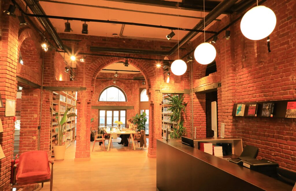 Traveletty - Visiting Libraries While Traveling - A young female tourist sitting in a cozy public library with brick walls located in Instanbul.