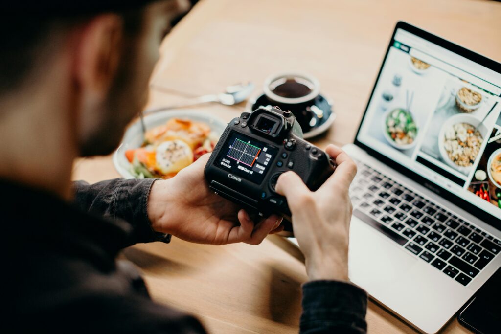 Traveletty - Budget Travel Food Tips - A male food travel blogger holding his DSLR camera while looking at a food website in his laptop