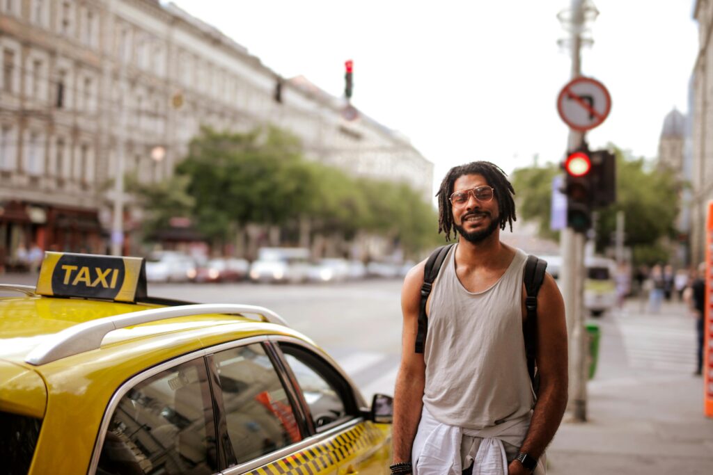 Traveletty - Budget Travel Transportation - A smiling male traveler standing beside a yellow cab