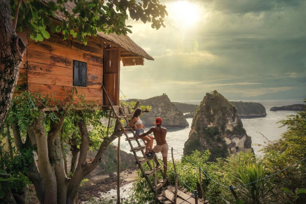 Traveletty - Romantic Travel Destination - couple sitting on a wooden ladder of a tree house while watching the beach view in Bali Indonesia