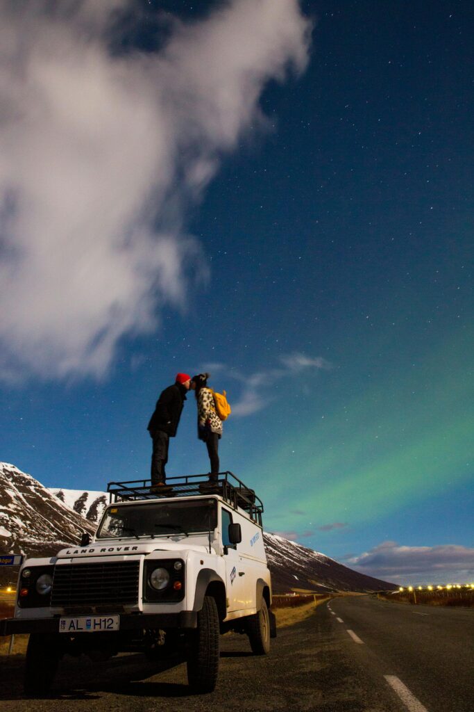 Traveletty - Romantic Travel Destination - couple kissing on top of a Land Rover truck with the beautiful night sky in Reykjavík, Iceland.