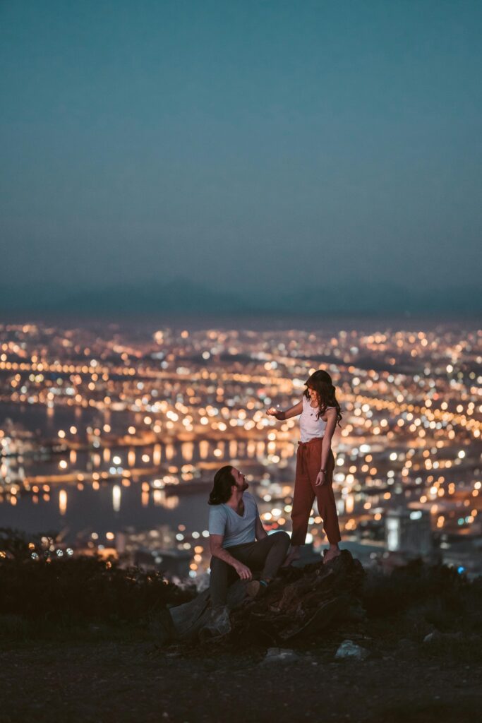 Traveletty - Romantic Travel Destination - couple posing at the top of a hill with the city lights of Cape Town, South Africa in the background